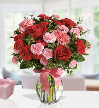 3 stems of Red Rose, 15 stems of Pink Carnation and 15 stems of Red Carnations with fillers in a glass vase. Shades Of Red & Pink